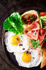 fried eggs with ham, salad and hummus on plate