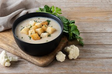 Cauliflower soup in a black bowl on wooden table. Copy space