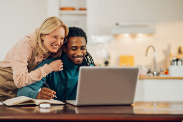 A cheerful woman is hugging and supporting her husband with his online job from home.