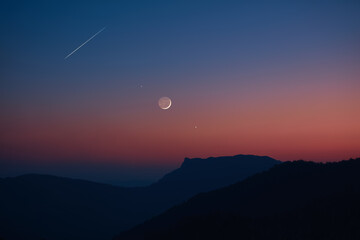 Silhouette of a countryside with Milky Way stars, shooting star, planets and crescent Moon.