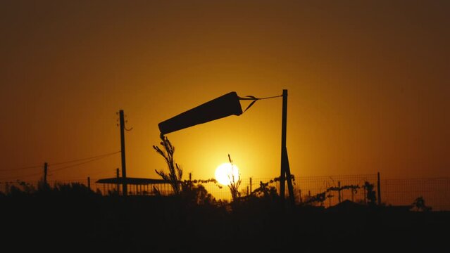 Dark silhouette of wind sock at orange sunset or dawn in field. Accurate weather forecast, summer wind direction. Windsock sways. Wind measurement. Meteorology, weather forecasting. Slow motion.
