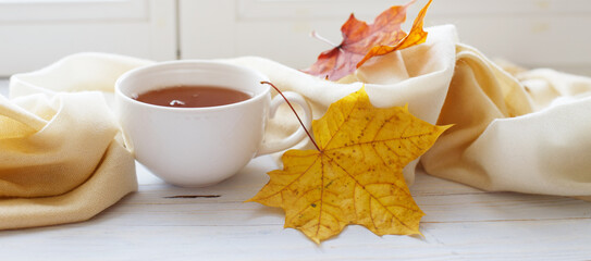 autumn leaves with a cup of tea or coffee next to a scarf on a wooden background banner