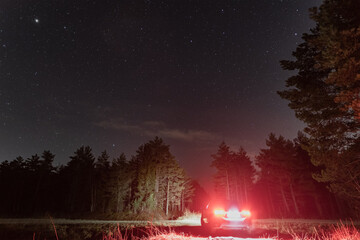 Night scene, car with headlights on, rear view, in a forest under a starry sky in autumn, low light photo.