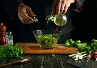 Experienced chef pours olive oil into a bowl of salad. Cooking delicious and healthy food with a set of vitamins in the kitchen