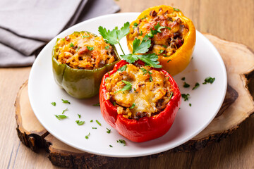 Stuffed peppers, halves of peppers stuffed with rice, dried tomatoes, herbs and cheese in a baking dish on a blue wooden table, top view. (Turkish name; biber dolmasi)