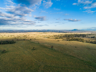 Aerial view of flat Aussie farm paddock with sunlight on grass and hills in distance