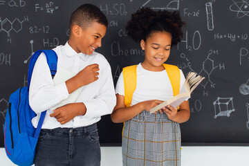 Happy African American schoolgirl and schoolboy solving problems near school board, back to school concept