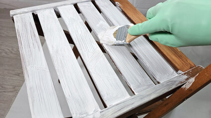 Close-up of a brush in hand and painting a wooden chair with white paint