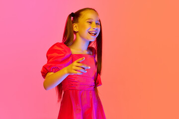 Laughing little girl in summer dress with ponytails posing over pink neon background. Concept of childhood, emotions, kids fashion