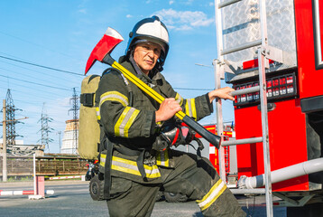 A firefighter wearing a helmet and protective clothing with a breathing apparatus holds an axe on...