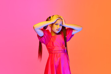 Shocked little girl in festive dress with ponytails posing over pink neon background. Concept of...