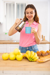 Woman holding coffee pot and pouring fresh coffee into mug. Woman having breakfast with hot drink at home