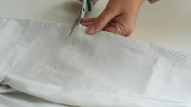Shortening jeans. White jeans, Measuring tape, scissors on table. Jeans cutting. Hands cut off the legs of jeans with scissors