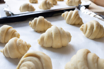 Close up of fluffy leavened uncooked traditional French croissants dough in a baking tray over paper sheet before put in oven. It's a buttery, flaky pastry of Austrian - Powered by Adobe