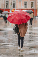Abstract hurrying girl under umbrella, back view, rainy evening, lifestyle in modern city, autumn weather