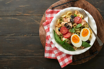 Italian pasta salad. Orecchiette pasta with tuna, tomato cherry, olive, basil and parmesan cheese in plate on dark wooden old rustic table background. Traditional Italian cuisine. Flat lay. Copy space