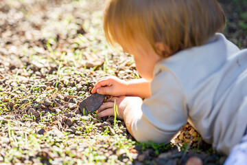 Baby girl lying on ground in gravel playing with rocks