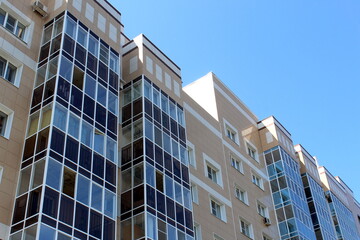 A high-rise multi-storey brick house stands against a blue sky, photo from bottom to top.