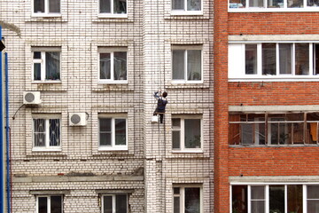On the facade of the house a man is hanging on a cable for repairs.
