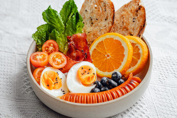 Breakfast bread, bacon, boiled eggs and fruits and vegetables.