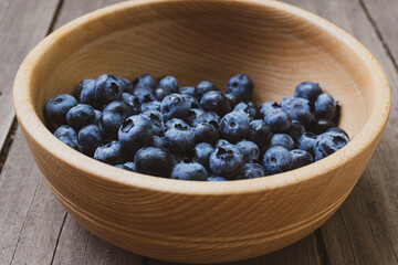 Wooden textured bowl with ripe blueberries inside.