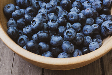 Lots of fresh large blueberries in a deep wooden plate.