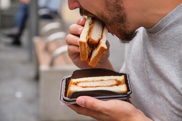 Unrecognizable man eating katsu sando, Japanese sandwich with pork cutlet, cabbage and tonkatsu...