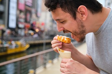 Tourist eating mitarashi dango, traditional Japanese rice dumplings smothered in a sweet soy glaze,...