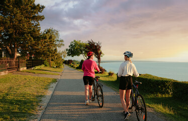 Obraz premium Two women walking on the sea promenade with bicycle. Back view.