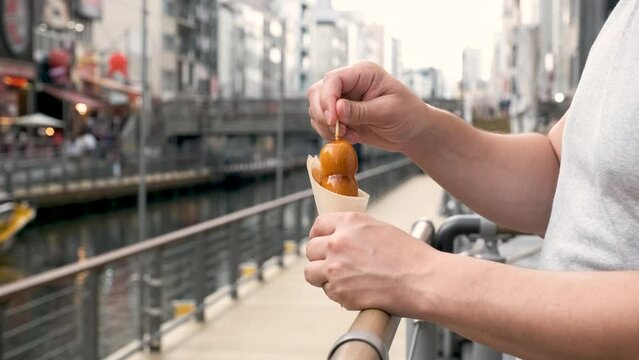 Tourist eating mitarashi dango, traditional Japanese rice dumplings smothered in a sweet soy glaze, at street.
