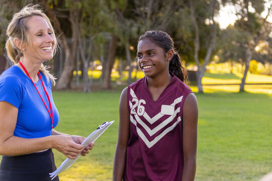 blonde woman holding clipboard coaching aboriginal football player
