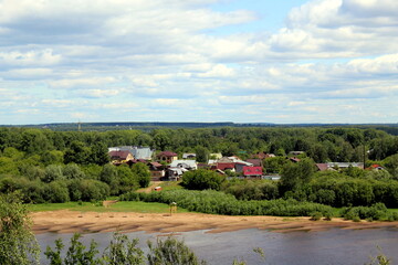 Beautiful view of the flowing river in summer with trees and fields and village houses.