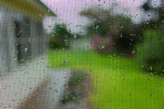 raindrops on fly screen gauze of rural houses veranda with garden out of focus behind