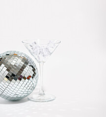 A glittering disco ball and alcoholic beverage glass with ice. Copy space for text. Night alcohol party.