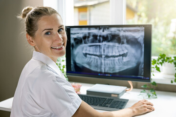 smiling dentist working with dental x-ray image on computer in clinics office