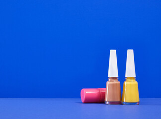 Colorful brightly colored nail polishes on a blue background. Copy space for text.
