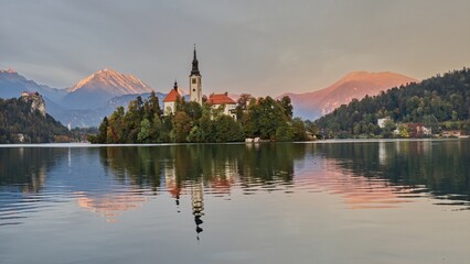 A church in the middle of Lake Bled with mountains on the horizon illuminated by the morning sun, Slovenia