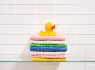A yellow duck sits on clean washed multicolored towels. Laundry day on weekend.