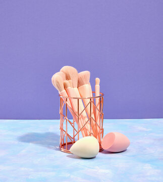 Beautiful makeup brushes in different sizes of nude colors stand in a interesting stand on the table. Cosmetic makeup sponges.