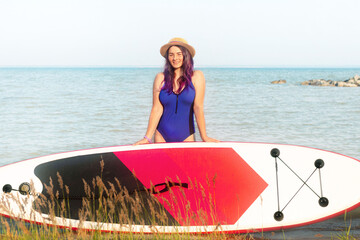 Sup boarding. A woman in a hat poses standing with a sup board. The concept of active lifestyle and...