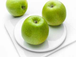 Three green apples on white plates on a white background separately from each other. Simple still life. Horizontal. Studio shot.