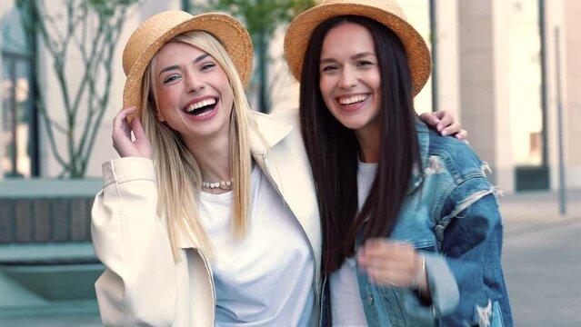 Two young beautiful blond smiling hipster women in trendy summer jeans clothes. Carefree women posing in street. Positive models having fun in hat