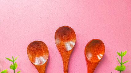 Set of wooden spoon three-piece isolated on pink background. Concept: kitchen utensils made from natural materials with beautiful glossy dark brown wood.