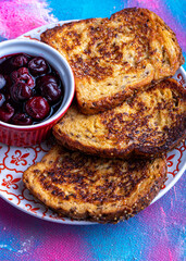 Toasted French toasts with cherry jam on a plate with a decorative pattern.