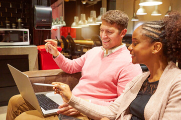 portrait two multiracial young adult business people sitting chatting working with a laptop in a sofa