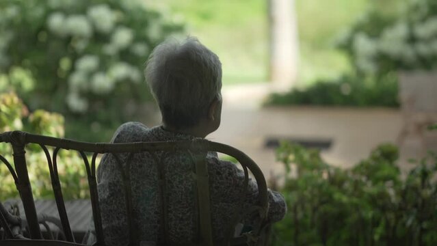 back of old elderly elder senior woman sitting resting relaxing on patio looking at garden