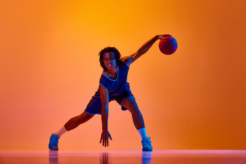 Young muscular man, athlete in motion, playing basketball, doing dribbling against orange background in neon lights. Concept of professional sport, competition, hobby, game, competition, ad © master1305