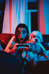 Close up portrait of A gamer or a streamer girl at home in a dark room with a game controller playing with her dog and sits in front of a monitor or TV.