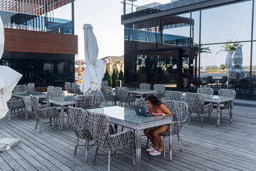 Cute young woman in swimsuit working on laptop sitting on terrace on the beach