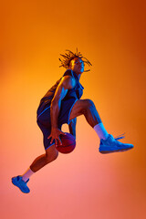 Fototapeta na wymiar Slam dunk position. Athletic young man, basketball player in motion with ball against orange background in neon lights. Concept of professional sport, competition, hobby, game, competition, ad